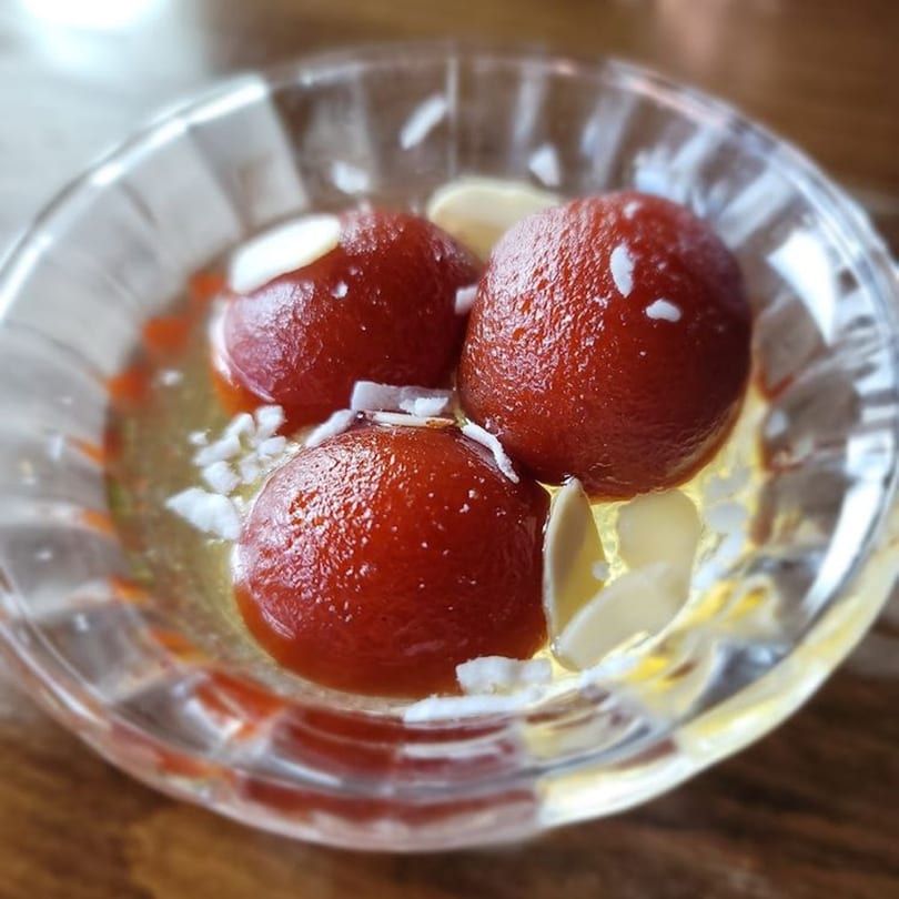Three Gulab Jamun, Indian fried dough balls, in syrup with almond slivers in a glass bowl.