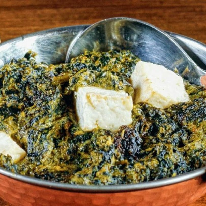 Close-up of Mountain Bites' Saag Paneer, a vibrant green spinach dish with white paneer cheese cubes.