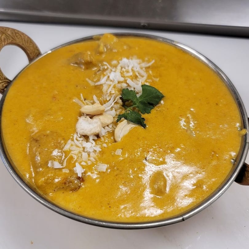 Indian Nepali chicken curry in a metal bowl, garnished with cashews, shredded coconut, and cilantro.