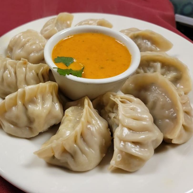 A plate of steamed Nepali momos with a side of orange dipping sauce garnished with cilantro.