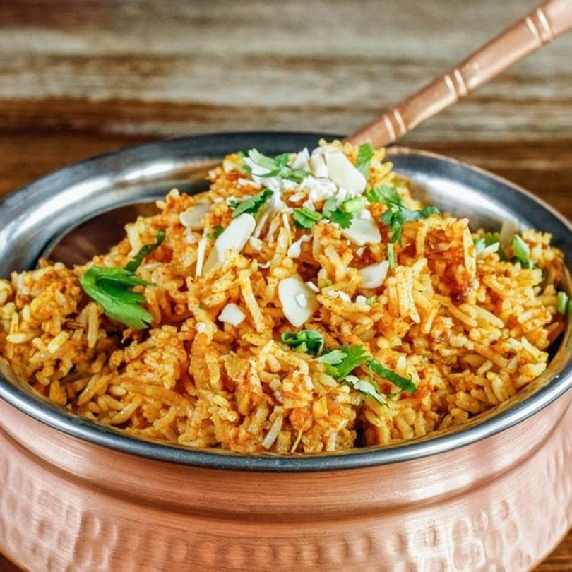 Indian Nepali Eatery's biryani, a copper bowl of rice with cilantro, almonds, and spices.